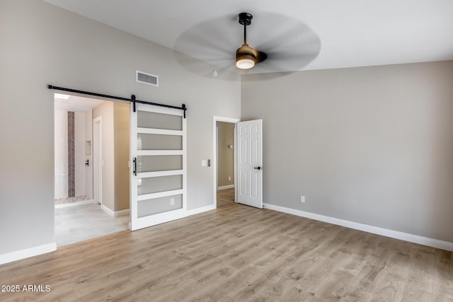 unfurnished room with a ceiling fan, visible vents, light wood finished floors, and a barn door