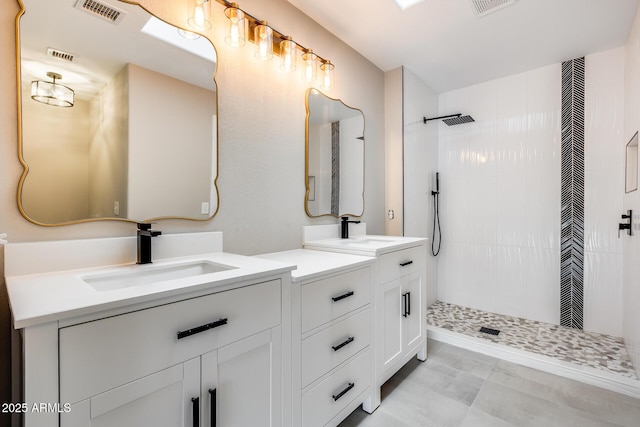 full bath featuring tiled shower, vanity, and visible vents