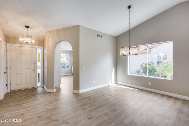 foyer entrance with arched walkways, light wood-style flooring, a notable chandelier, visible vents, and vaulted ceiling