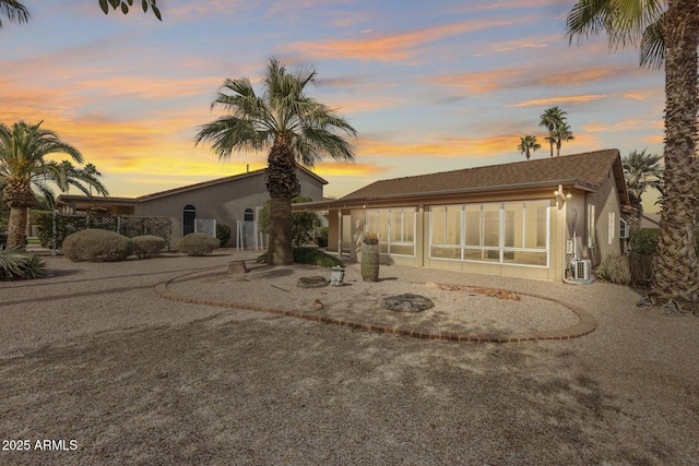 back of house at dusk with a sunroom and stucco siding