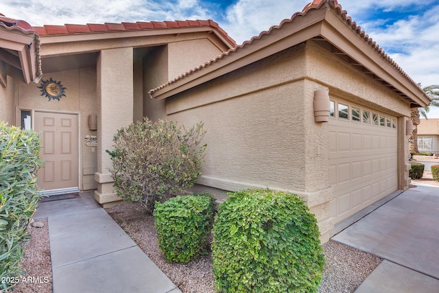 property entrance featuring driveway, an attached garage, a tile roof, and stucco siding