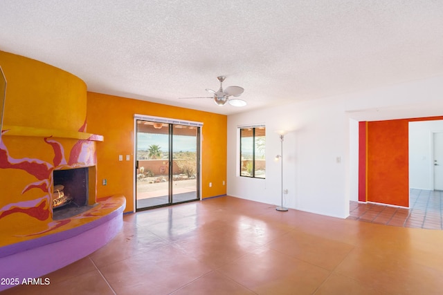 unfurnished living room with tile patterned flooring, a warm lit fireplace, ceiling fan, and a textured ceiling