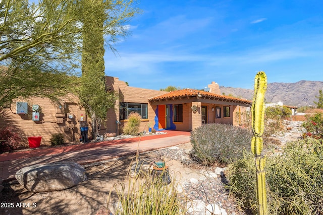 adobe home featuring a patio, a chimney, a mountain view, and a tiled roof