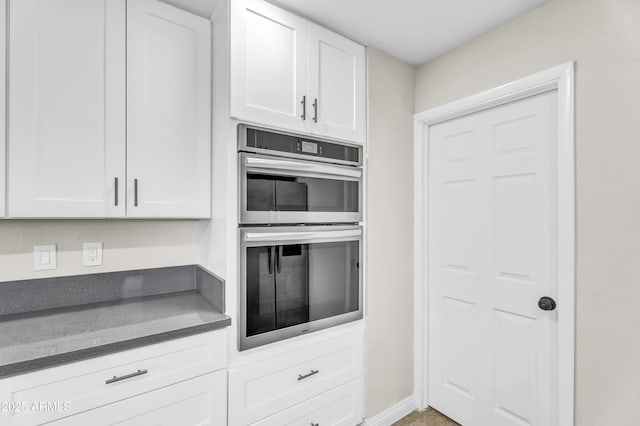 kitchen with dark countertops, baseboards, white cabinetry, and stainless steel double oven