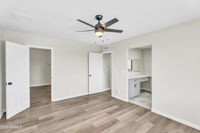 unfurnished bedroom with light wood finished floors, baseboards, visible vents, and a walk in closet