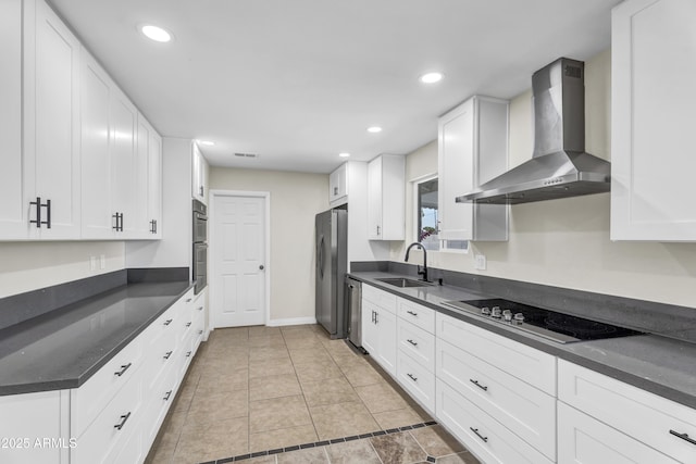 kitchen featuring dark countertops, wall chimney exhaust hood, appliances with stainless steel finishes, white cabinetry, and a sink