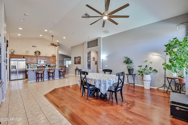 dining area featuring arched walkways, ceiling fan, high vaulted ceiling, light wood-style flooring, and visible vents