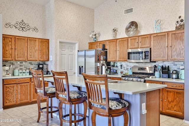 kitchen featuring visible vents, a kitchen island with sink, a high ceiling, stainless steel appliances, and light countertops