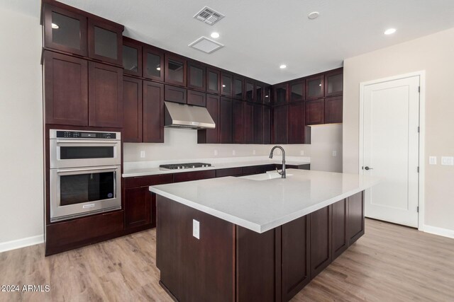 kitchen featuring sink, stainless steel double oven, gas cooktop, light hardwood / wood-style flooring, and a center island with sink