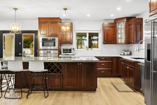 kitchen with an inviting chandelier, stainless steel appliances, hanging light fixtures, and light hardwood / wood-style flooring