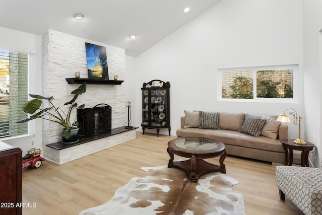 living room with a stone fireplace, high vaulted ceiling, and light hardwood / wood-style flooring