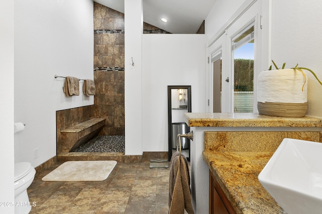 bathroom with tiled shower, lofted ceiling, toilet, and sink