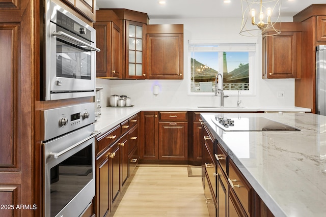 kitchen with sink, hanging light fixtures, black electric cooktop, light stone countertops, and light hardwood / wood-style floors