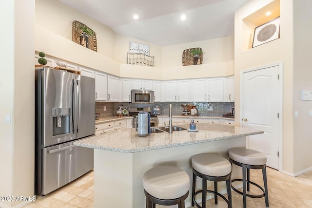 kitchen with stainless steel appliances, a breakfast bar, a sink, white cabinets, and backsplash