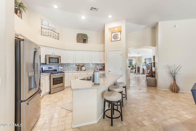 kitchen featuring arched walkways, a sink, a towering ceiling, visible vents, and appliances with stainless steel finishes