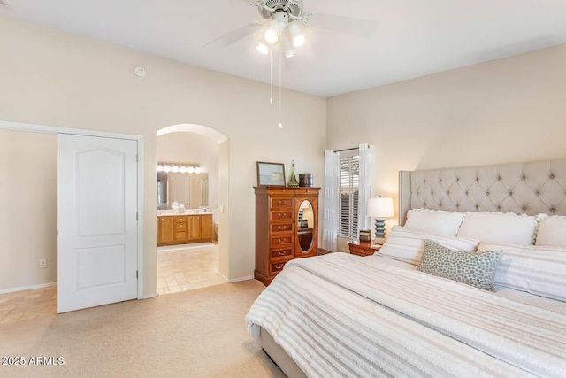 bedroom with arched walkways, light colored carpet, connected bathroom, ceiling fan, and baseboards