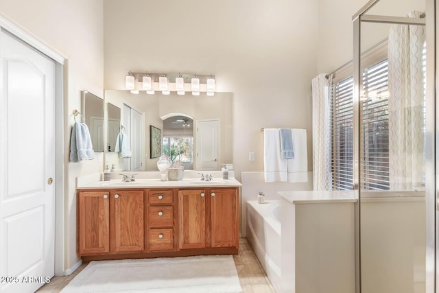 full bath featuring a healthy amount of sunlight, a garden tub, double vanity, and a sink