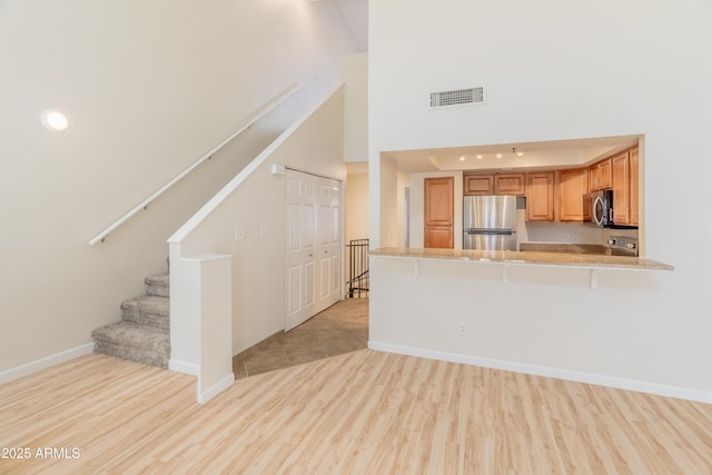 unfurnished living room with baseboards, a high ceiling, visible vents, and light wood-style flooring