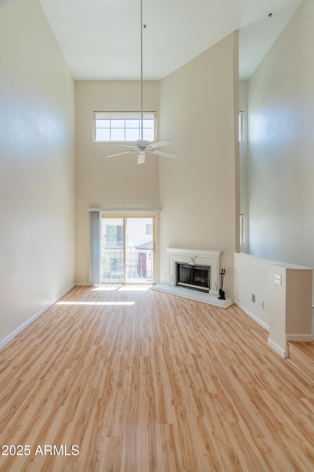 unfurnished living room with baseboards, a fireplace with raised hearth, ceiling fan, and wood finished floors