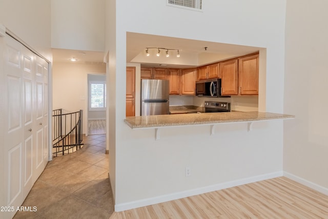 kitchen featuring visible vents, a peninsula, a breakfast bar, baseboards, and stainless steel appliances