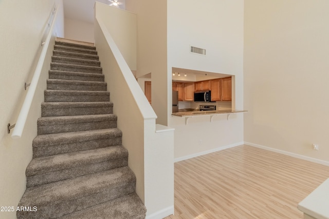 stairs featuring baseboards, visible vents, wood finished floors, and a towering ceiling