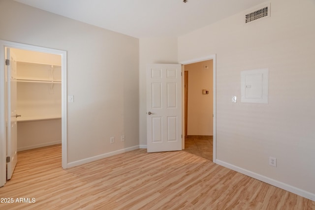 unfurnished bedroom featuring visible vents, a closet, baseboards, a walk in closet, and light wood-style flooring