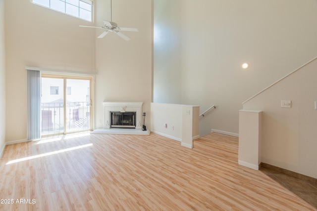 unfurnished living room featuring baseboards, a fireplace with raised hearth, light wood finished floors, and a towering ceiling