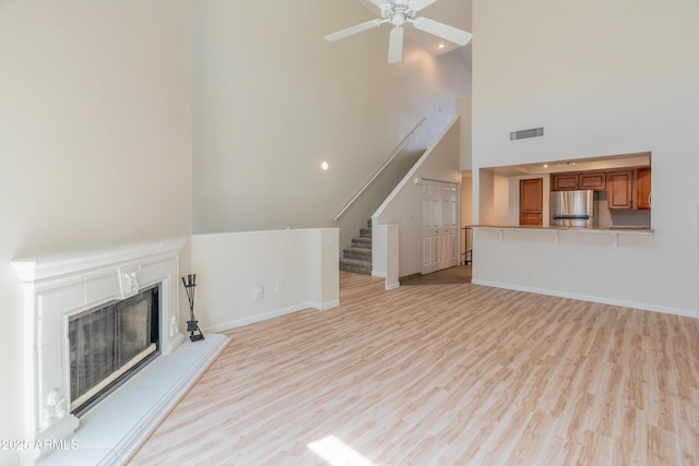 unfurnished living room with a fireplace with raised hearth, stairs, baseboards, light wood-type flooring, and visible vents