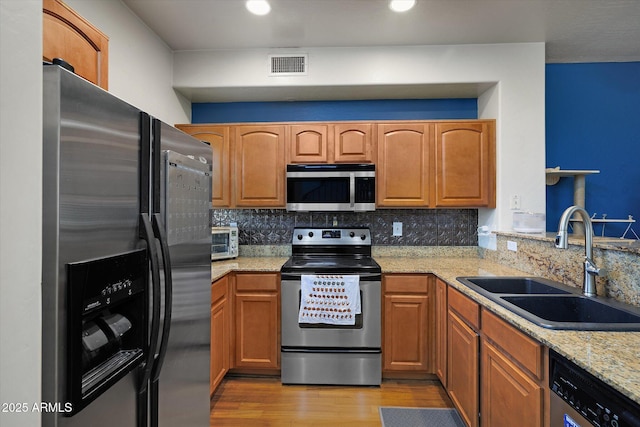 kitchen featuring appliances with stainless steel finishes, brown cabinetry, a sink, and visible vents