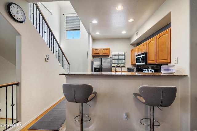 kitchen featuring a peninsula, appliances with stainless steel finishes, dark stone countertops, and a kitchen bar