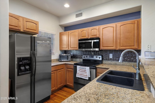 kitchen featuring light stone counters, stainless steel appliances, a sink, visible vents, and decorative backsplash