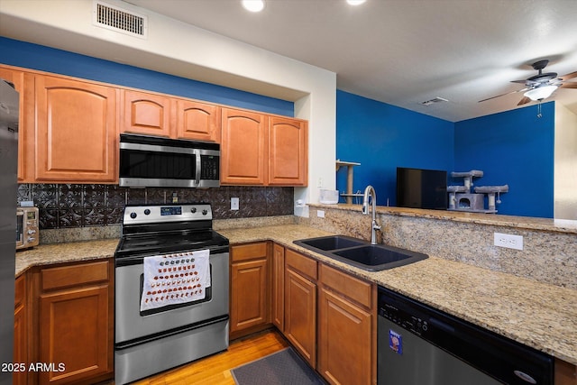 kitchen with light stone countertops, stainless steel appliances, a sink, visible vents, and decorative backsplash