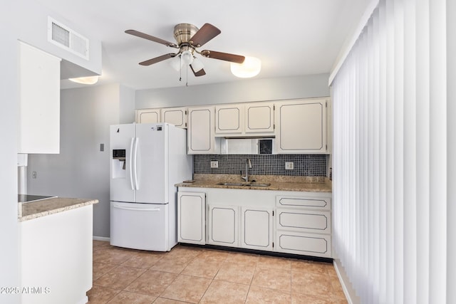 kitchen with tasteful backsplash, sink, white cabinets, white fridge with ice dispenser, and light tile patterned floors