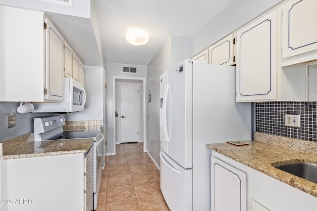 kitchen with light tile patterned flooring, white appliances, light stone countertops, and white cabinets