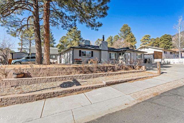 view of front of property featuring driveway, a chimney, and fence