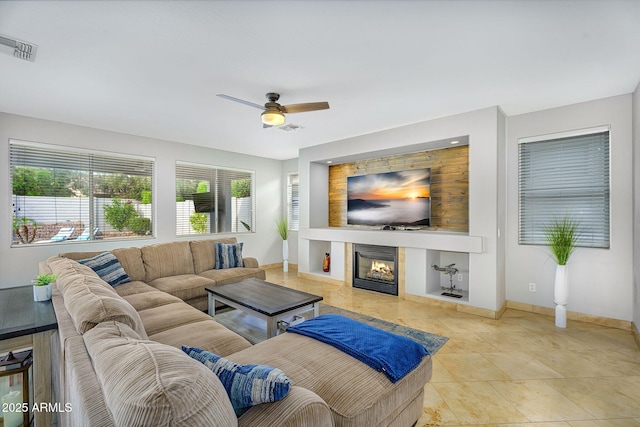 living room with a tiled fireplace, visible vents, baseboards, and ceiling fan