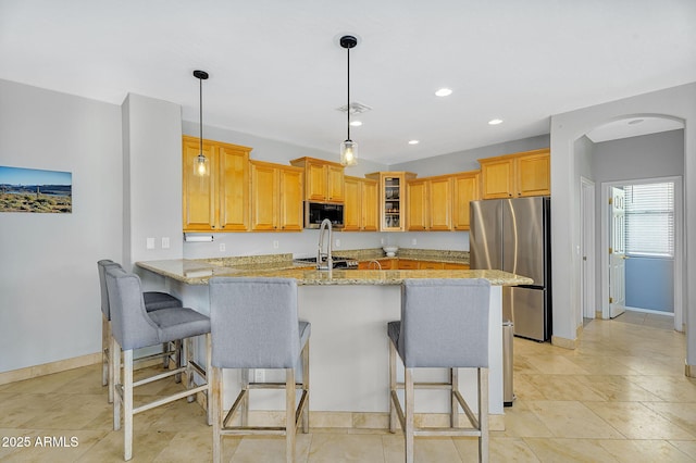 kitchen with a peninsula, stainless steel appliances, glass insert cabinets, light stone counters, and a kitchen breakfast bar