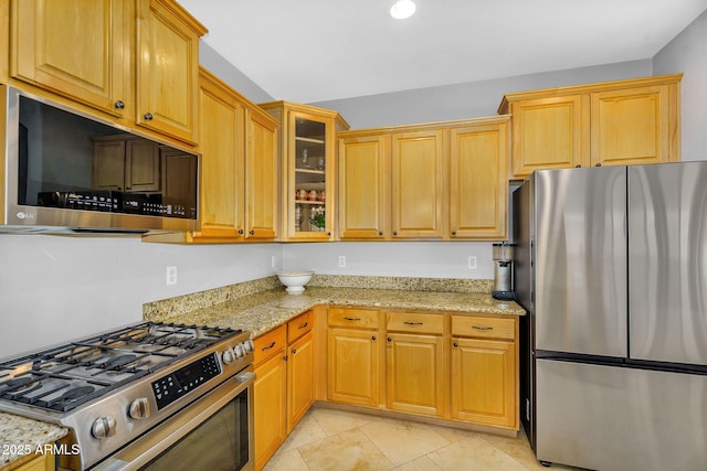 kitchen featuring light tile patterned floors, appliances with stainless steel finishes, light stone counters, and glass insert cabinets