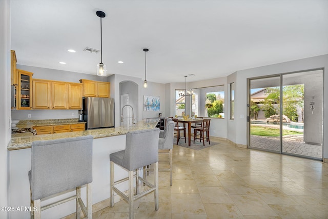 kitchen with visible vents, a breakfast bar, arched walkways, glass insert cabinets, and freestanding refrigerator