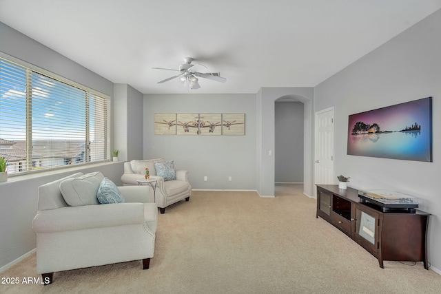 living area with light colored carpet, arched walkways, baseboards, and a ceiling fan