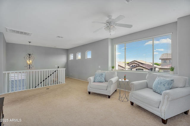 living area featuring ceiling fan with notable chandelier, light colored carpet, and visible vents