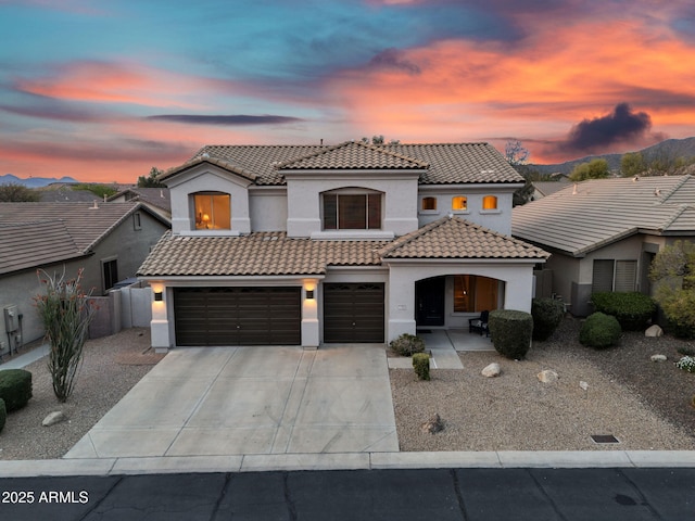 mediterranean / spanish home with driveway, stucco siding, fence, an attached garage, and a tiled roof