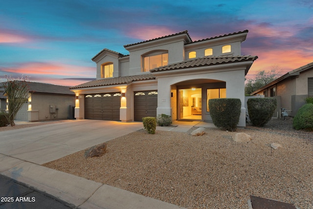 mediterranean / spanish home with a tile roof, stucco siding, an attached garage, and concrete driveway