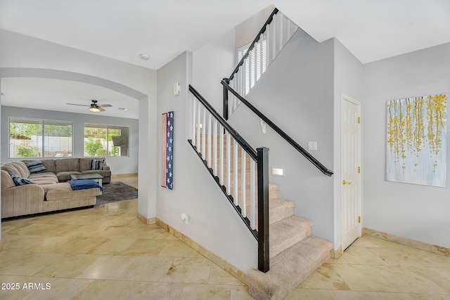 stairway featuring a ceiling fan, arched walkways, and baseboards