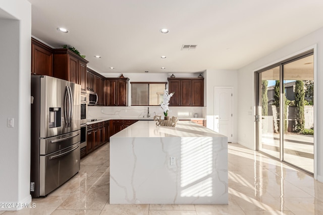 kitchen featuring light stone counters, dark brown cabinetry, stainless steel appliances, sink, and a kitchen island