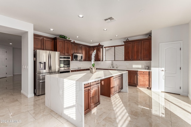 kitchen with light stone countertops, sink, a center island, backsplash, and appliances with stainless steel finishes