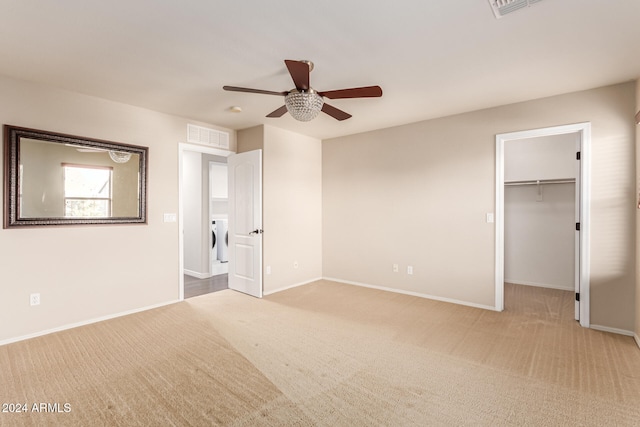 unfurnished bedroom with a walk in closet, ceiling fan, light colored carpet, washer / dryer, and a closet