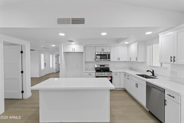 kitchen with stainless steel appliances, white cabinetry, a center island, and sink