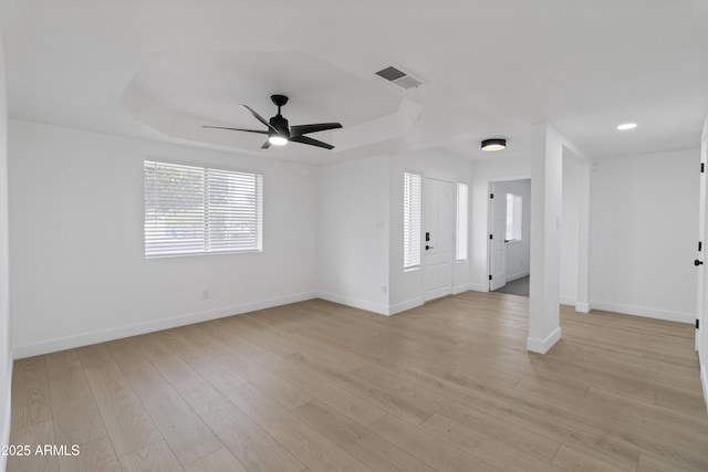 unfurnished room with a tray ceiling, light hardwood / wood-style flooring, and a wealth of natural light