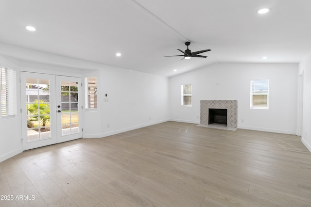 unfurnished living room with ceiling fan, a tiled fireplace, vaulted ceiling, french doors, and light wood-type flooring